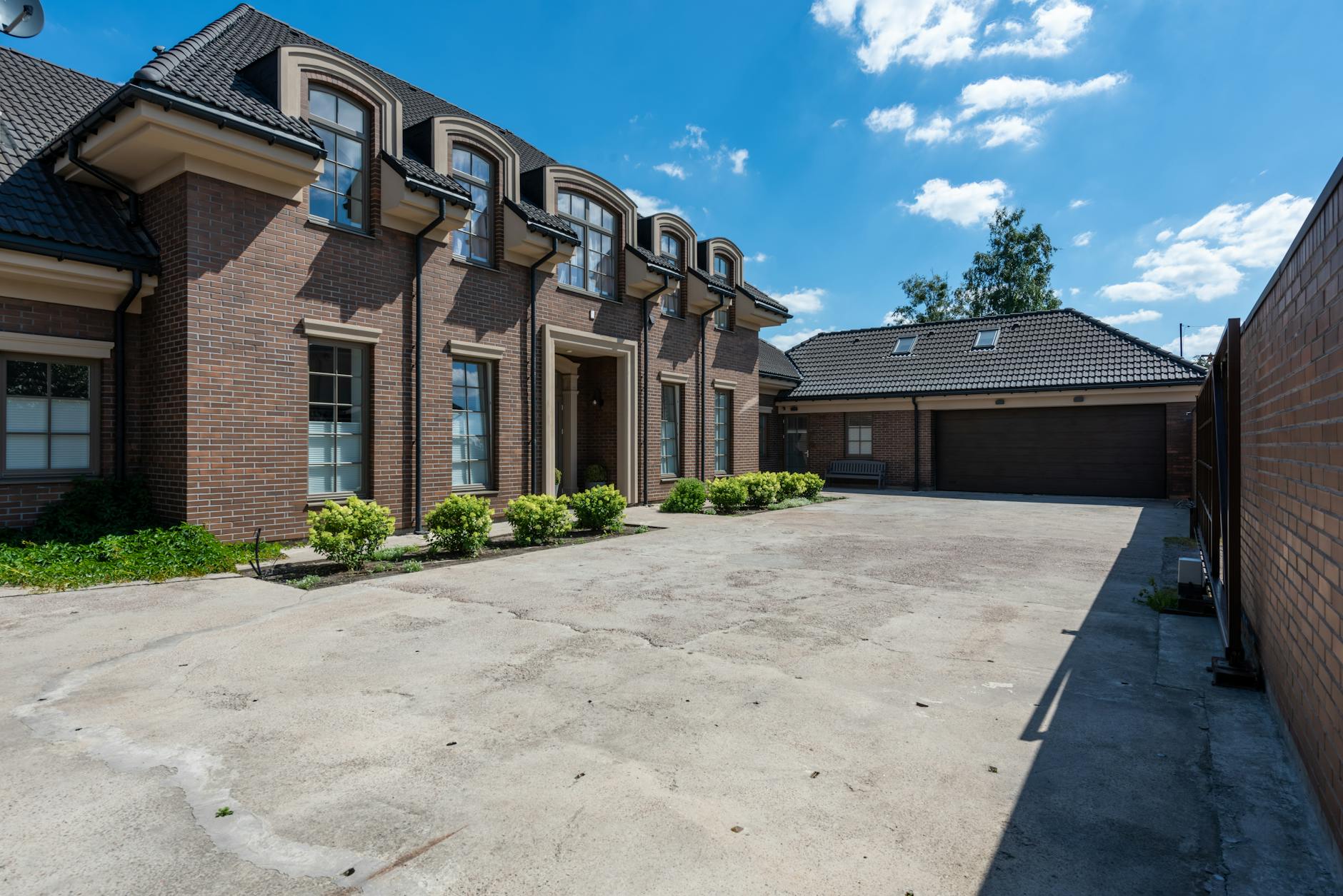 Elewacja murowanego domu jednorodzinnego w słońcu, szeroki podjazd