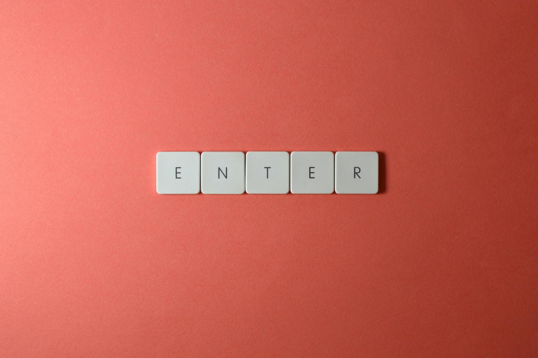 Kafelki klawiatury układające się w słowo ENTER na koralowym tle