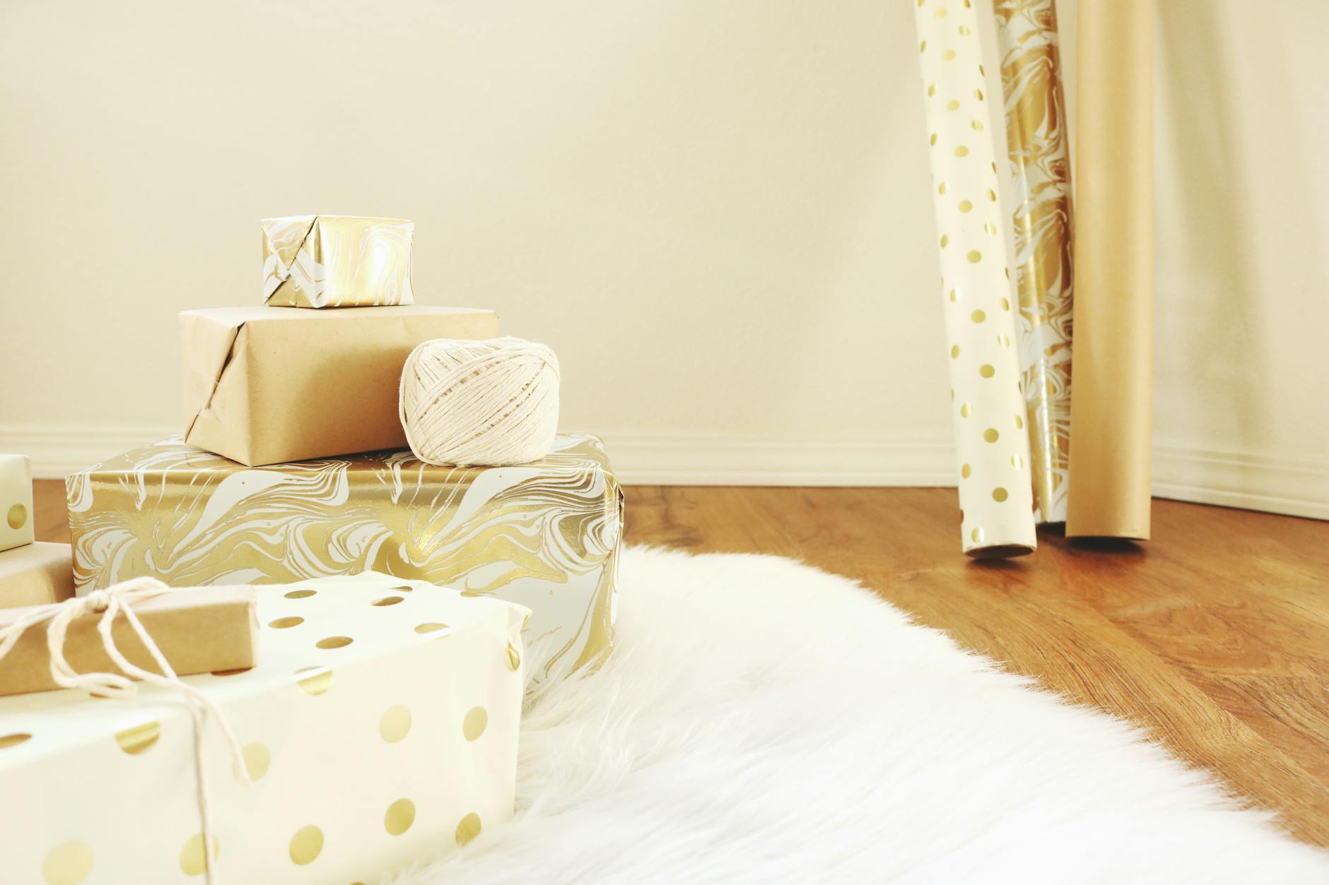 Stos elegancko zapakowanych złoto-białych prezentów na drewnianej podłodze