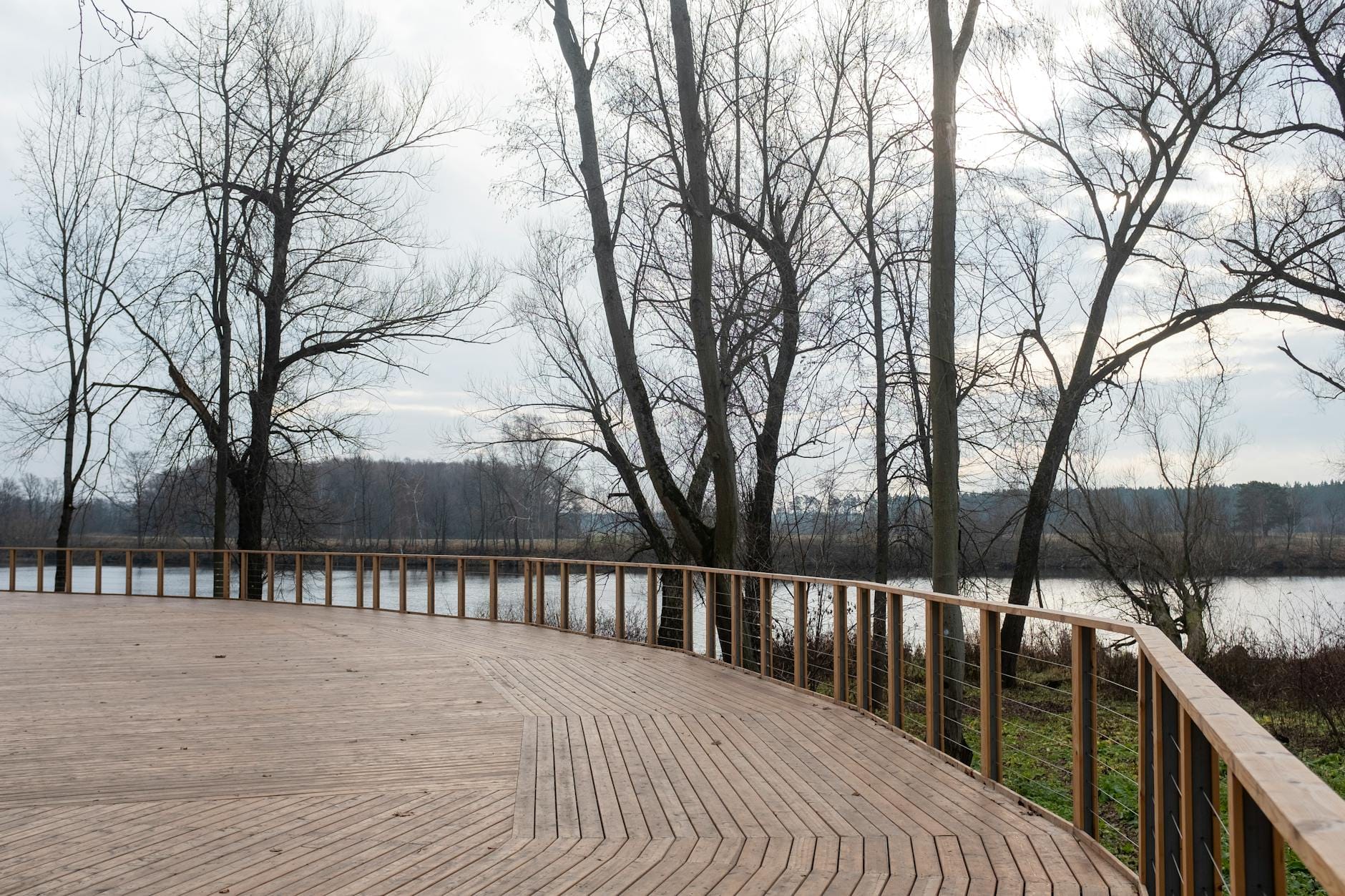 Drewniany taras zimą z widokiem na spokojne jezioro i bezlistne drzewa