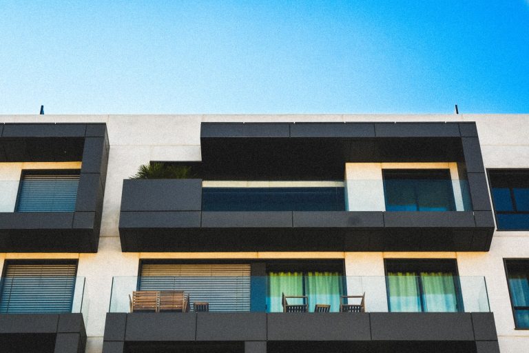 Szklana fasada apartamentowca z balkonami na tle błękitnego nieba